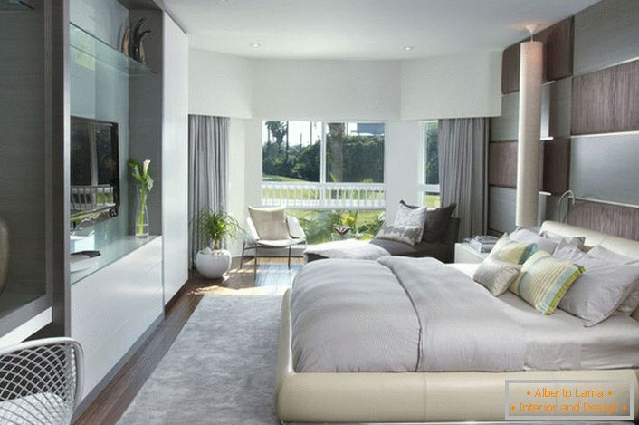Меко, насипно легло в спалнята в модерен стил. Мебелите с гланцова повърхност се вписват добре в цялостния състав на интериора.