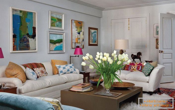 Универсална всекидневна в еклектичен стил. Уютната стая прави много възглавници и абстрактни, светли картини, които украсяват стената над дивана.