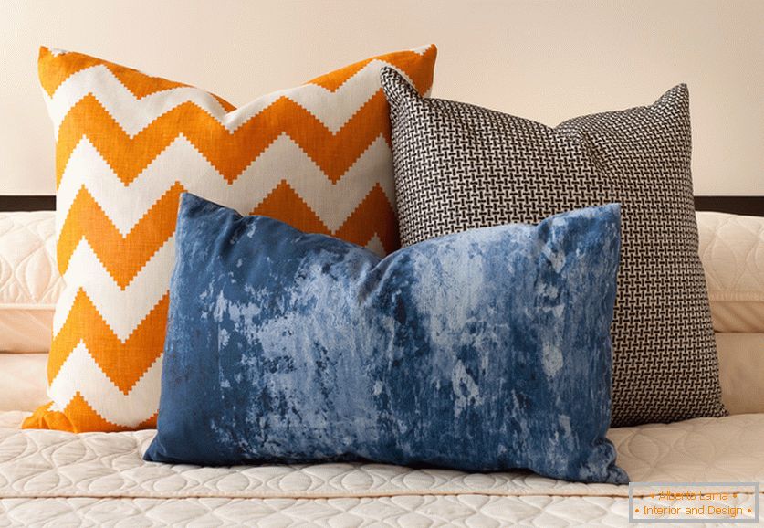 Светли оранжеви, сини и черно-бели декоративни възглавници с интересни отпечатъци върху леглото